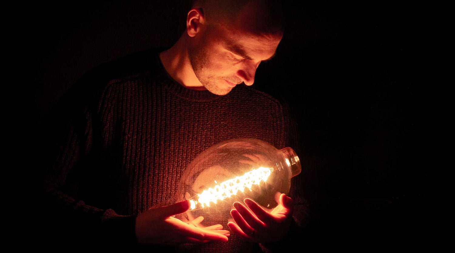 Emmet-Bosonnet-cradling-an-edison-fillament-bulb-like-a-baby-while-looking-down-on-it-dublin-ireland